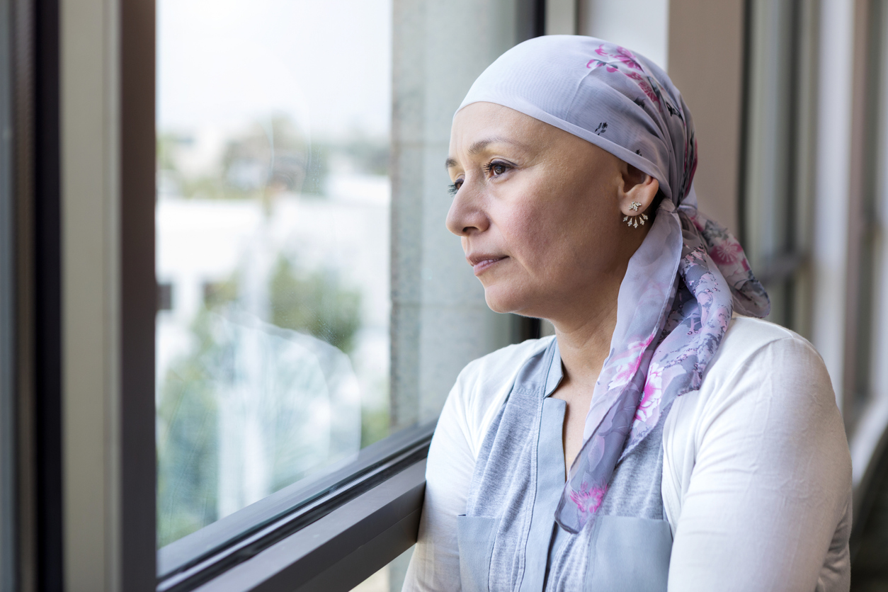 Thinking about her journey with breast cancer, a mature adult woman leans against the window and looks out.