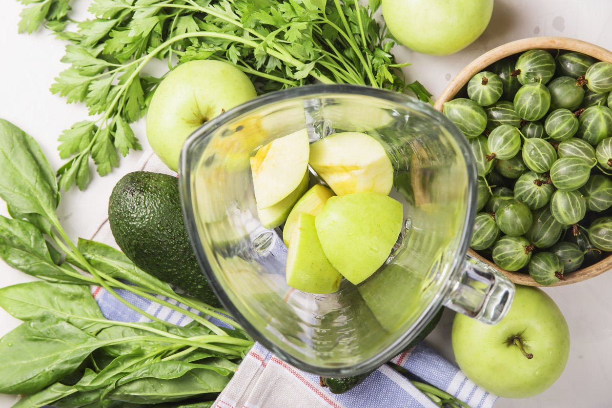 Ingredients for making healthy green smoothies made from apples, spinach, avocado and parsley around a blender glass bowl. Top view. flat lay