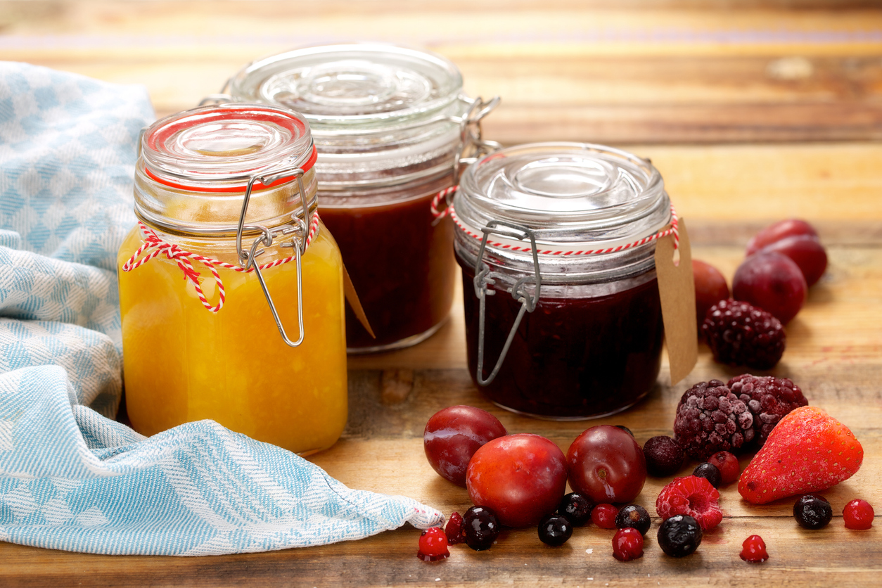 Glass jars with different kind of jam and berries on wooden background.