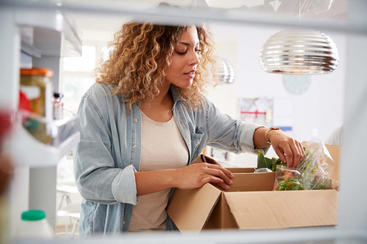 Woman unpacking her plant-based meal kit into fridge