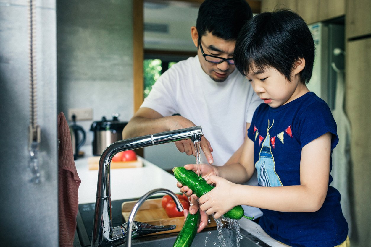 Cute child washing tomatoes and cucumbers.