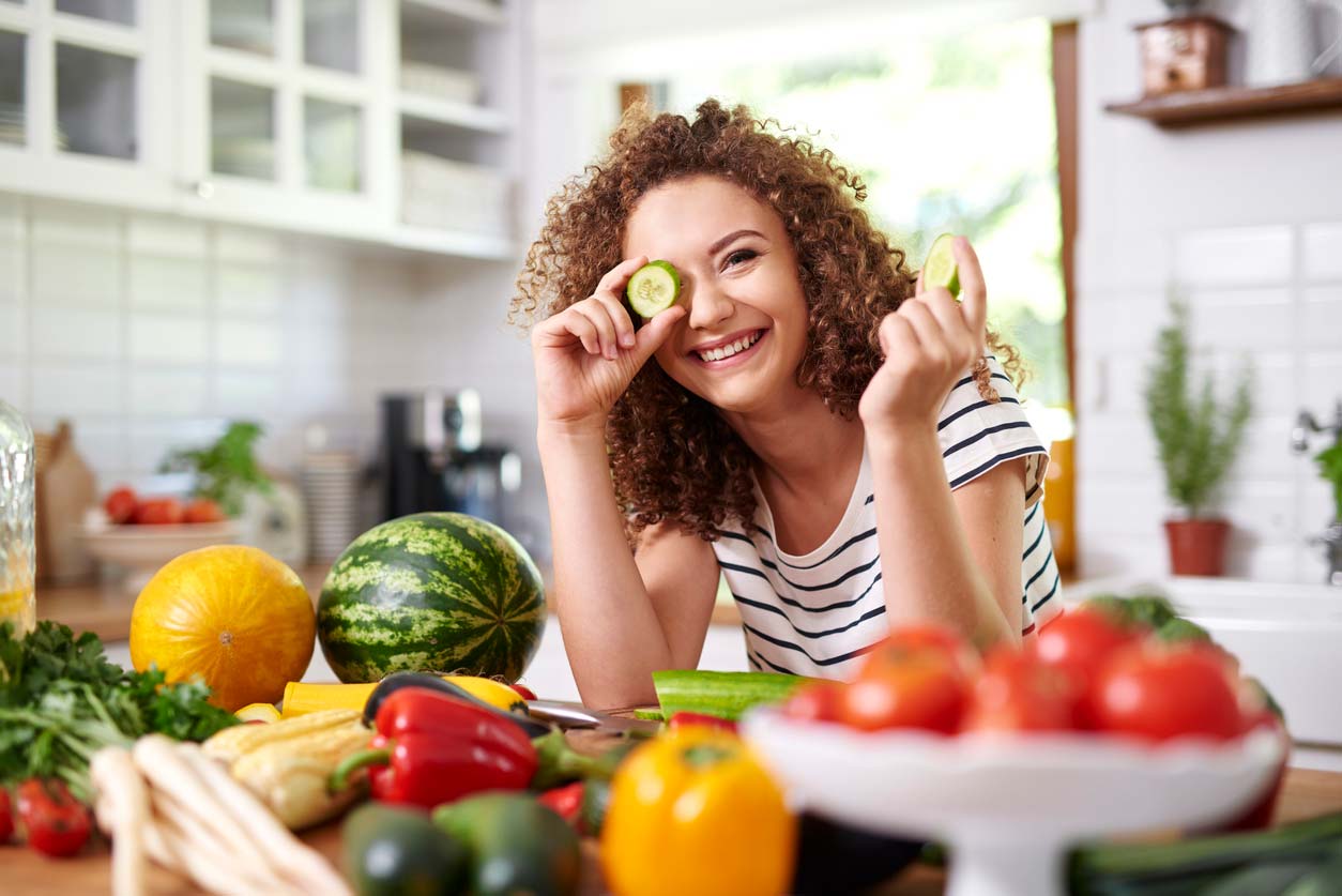Woman playfully holding cucumber slice in front of eye