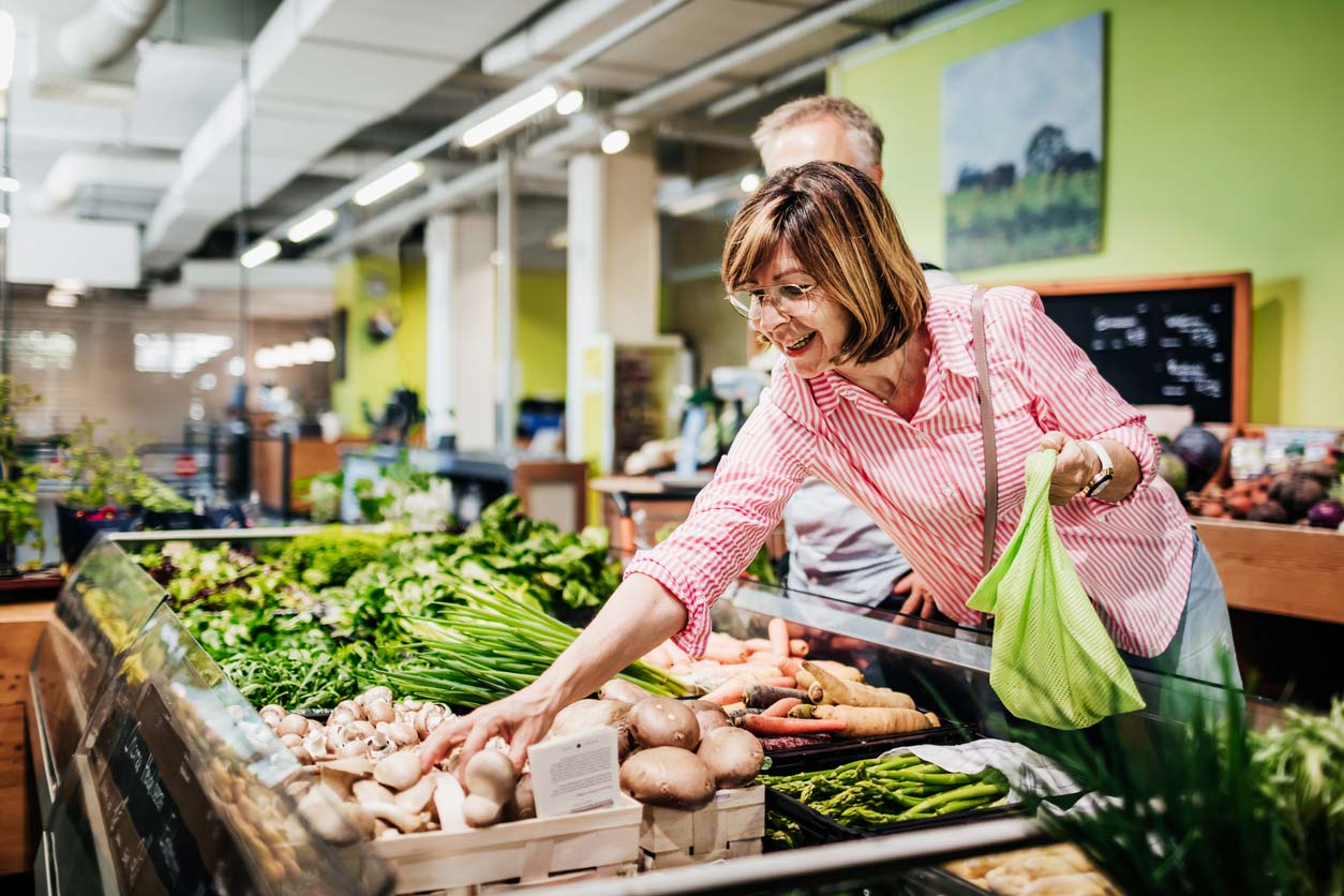 mature woman reaching for mushrooms in grocery store