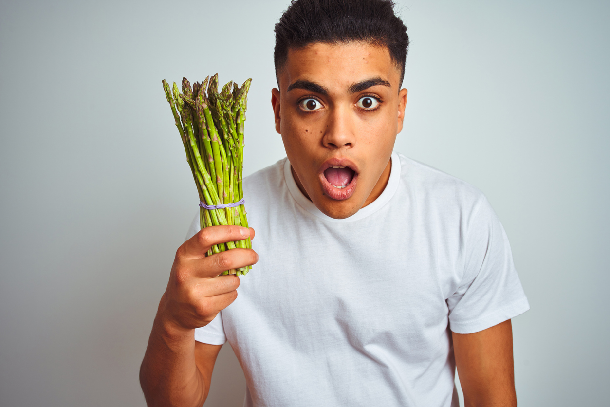 Young brazilian man eating asparagus standing over isolated grey background scared in shock with a surprise face, afraid and excited with fear expression