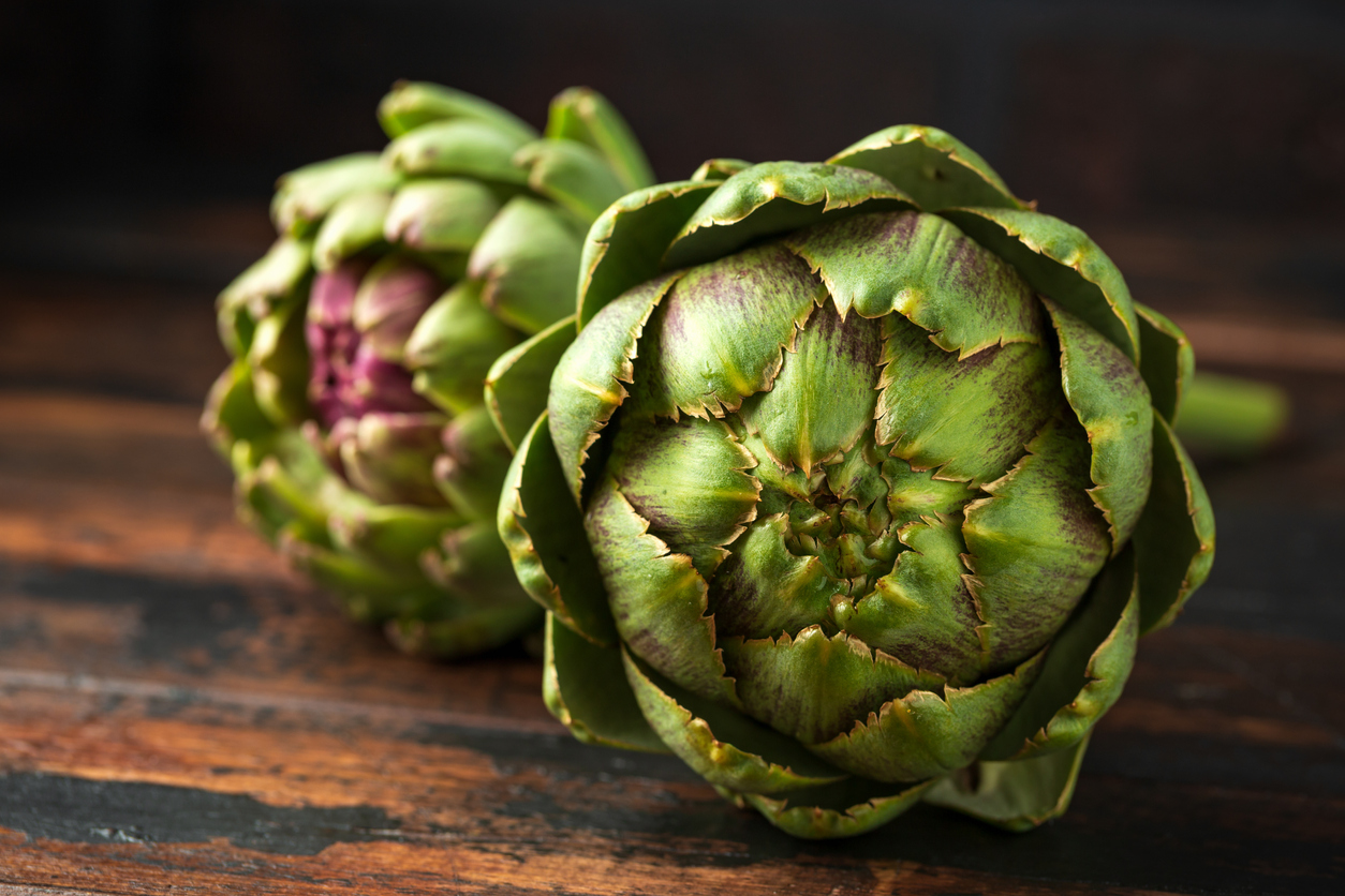 Fresh raw organically grown artichoke flower buds on wooden table.