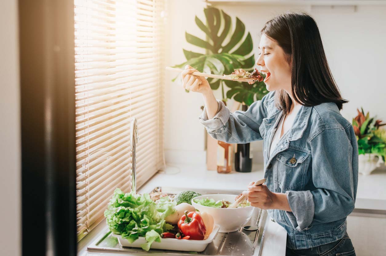 woman eating fresh vegetables while prepping healthy salads