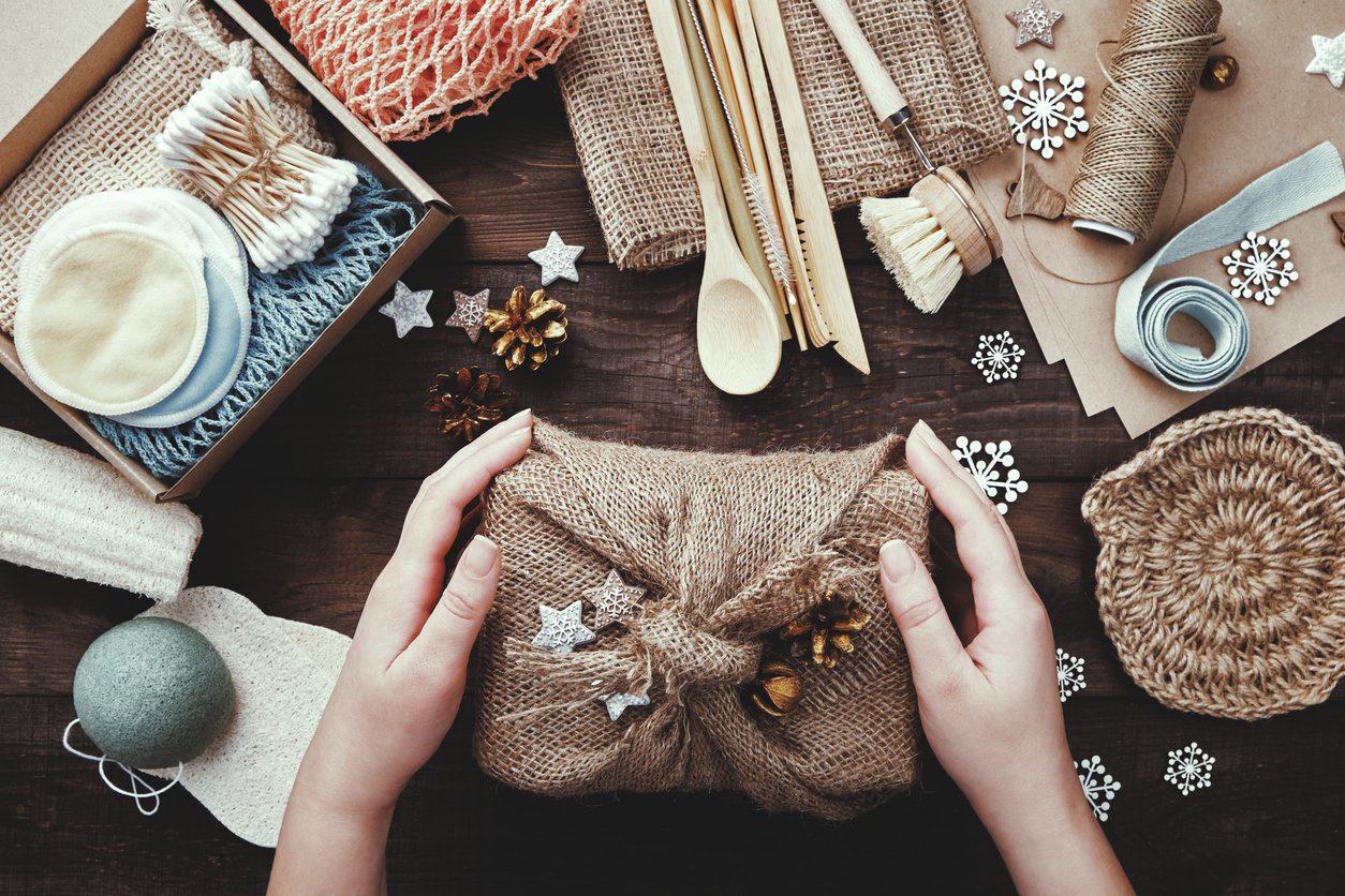 Zero waste christmas. Female hands pack gift wrapped in burlap. Eco friendly products laid out on table