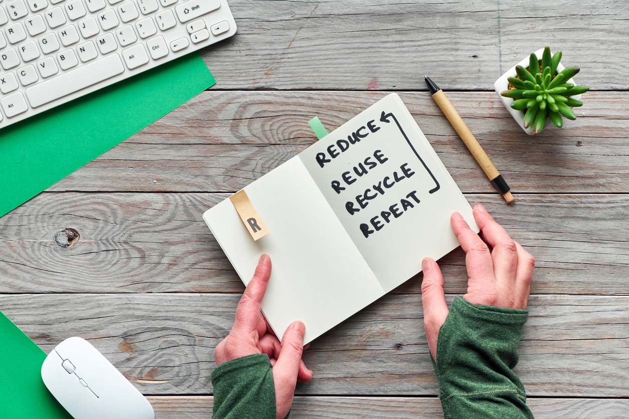 hands with notebook that says reduce reuse recycle repeat