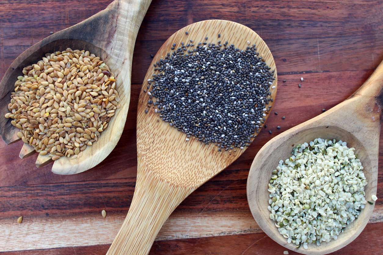 Wooden spoons filled with chia seeds, hemp seed hearts, and golden flax seeds on the wooden background. A concept of heart friendly super food.