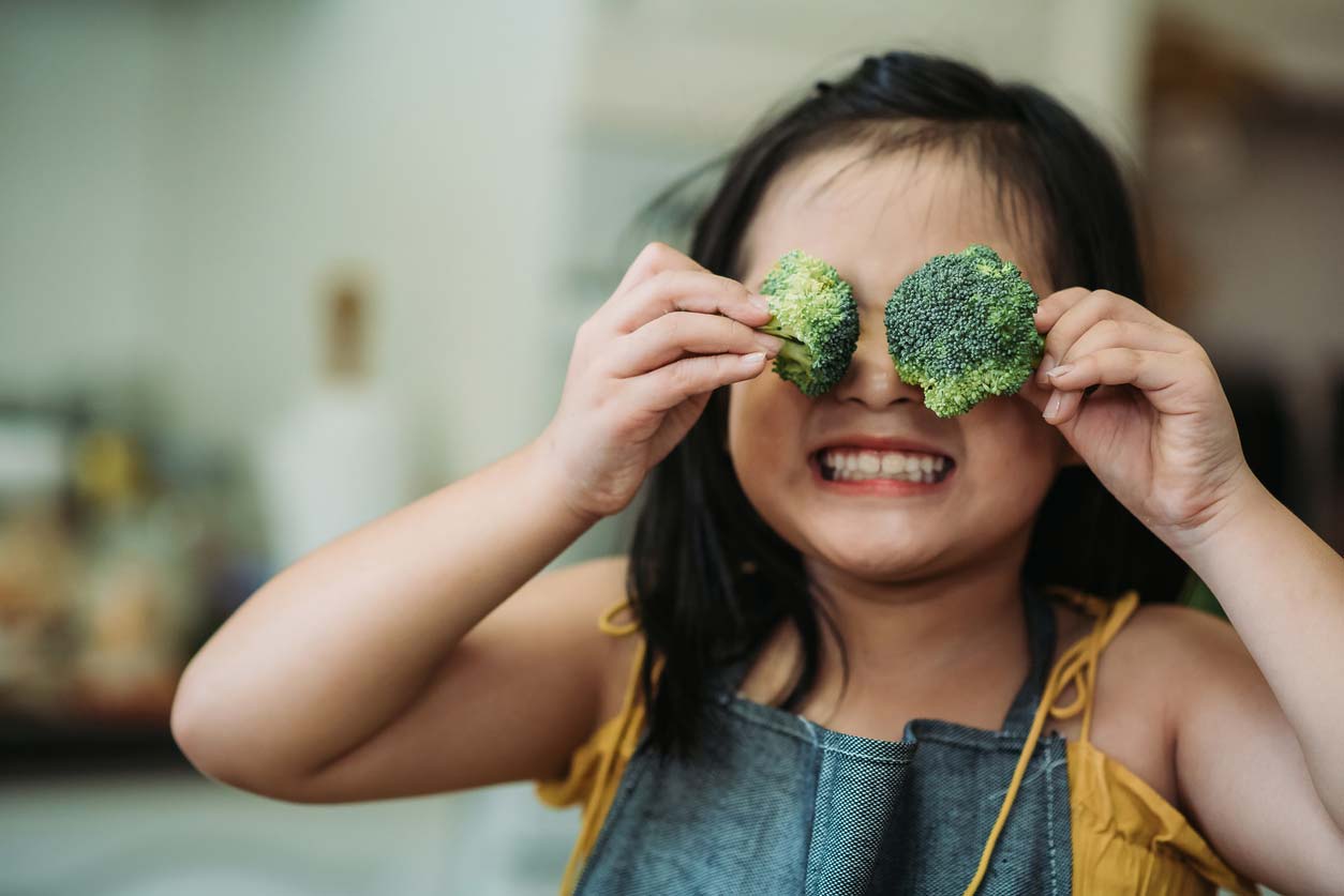 child holding broccoli in front of eyes