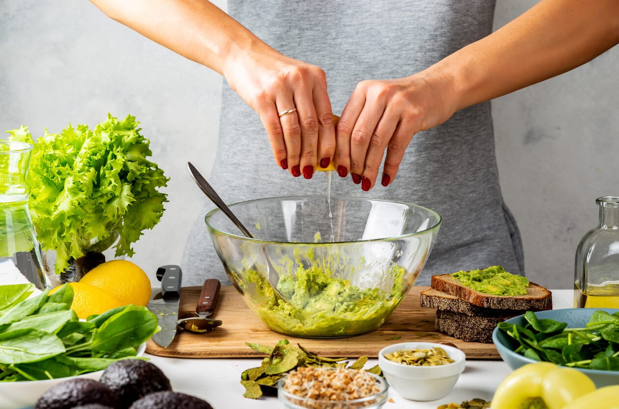 woman squeezes juice from a lemon in a glass bowl with avocado guacamole healthy