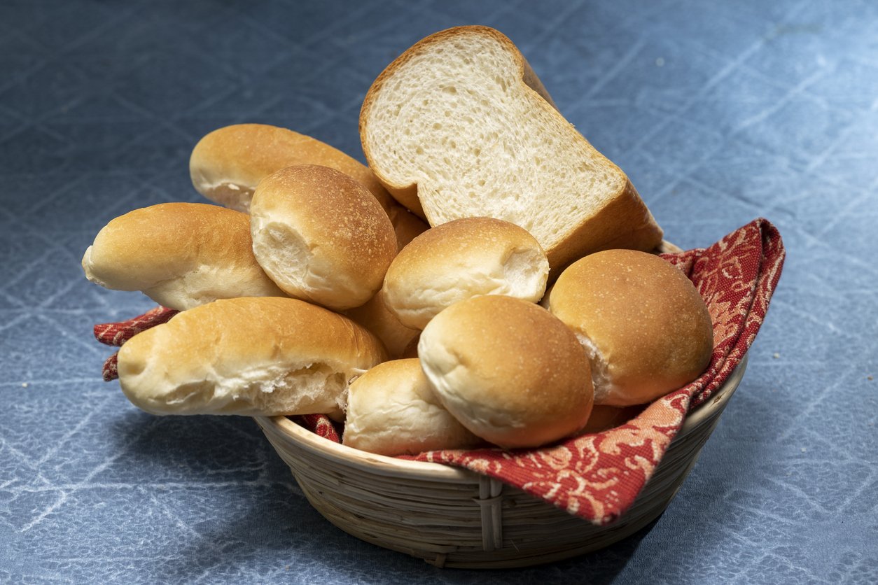 A professional Digita SLR photo of breadbasket with delicious crispy Austrian, German, Swiss buns. There are traditional buns inside the breadbasket. Breadbasket placed on a blue table mat with a red towel. Post processing with adobe Photoshop. shot taken using Canon camera.