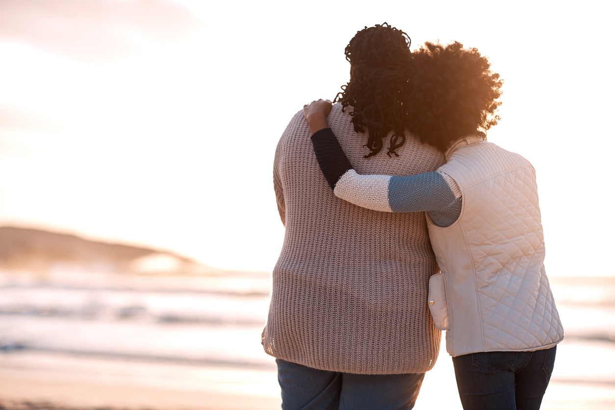 Rearview shot of a young woman embracing her mother while watching the sunset at the beach