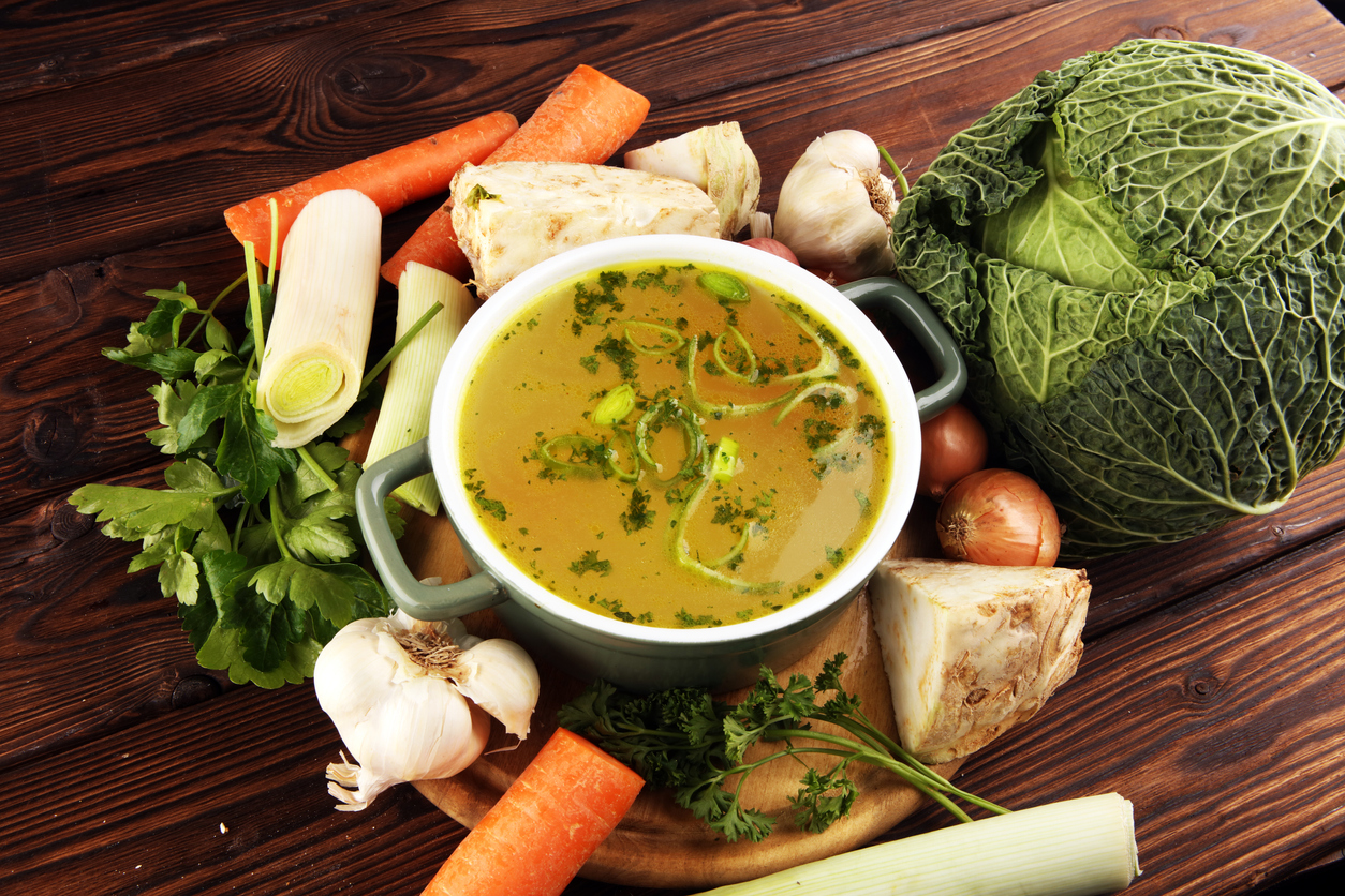 Broth with carrots, onions various fresh vegetables in a pot - colorful fresh clear spring soup. Rural kitchen scenery vegetarian bouillon