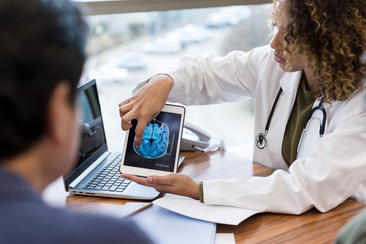 The mid adult female doctor holds the digital tablet displaying the brain scan and explains the test results to the unrecognizable male patient.