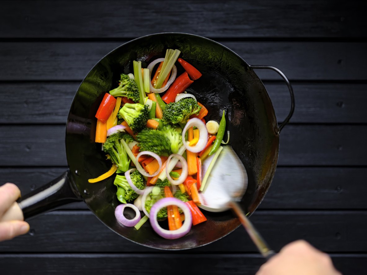 Stir frying and sauteing a variety of fresh colorful market vegetables in a hot wok.