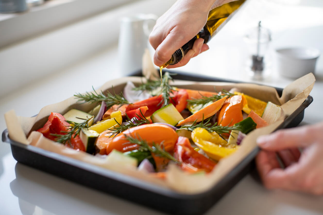 close-up of seasoning tray of vegetables for roasting with olive oil ready for vegan
