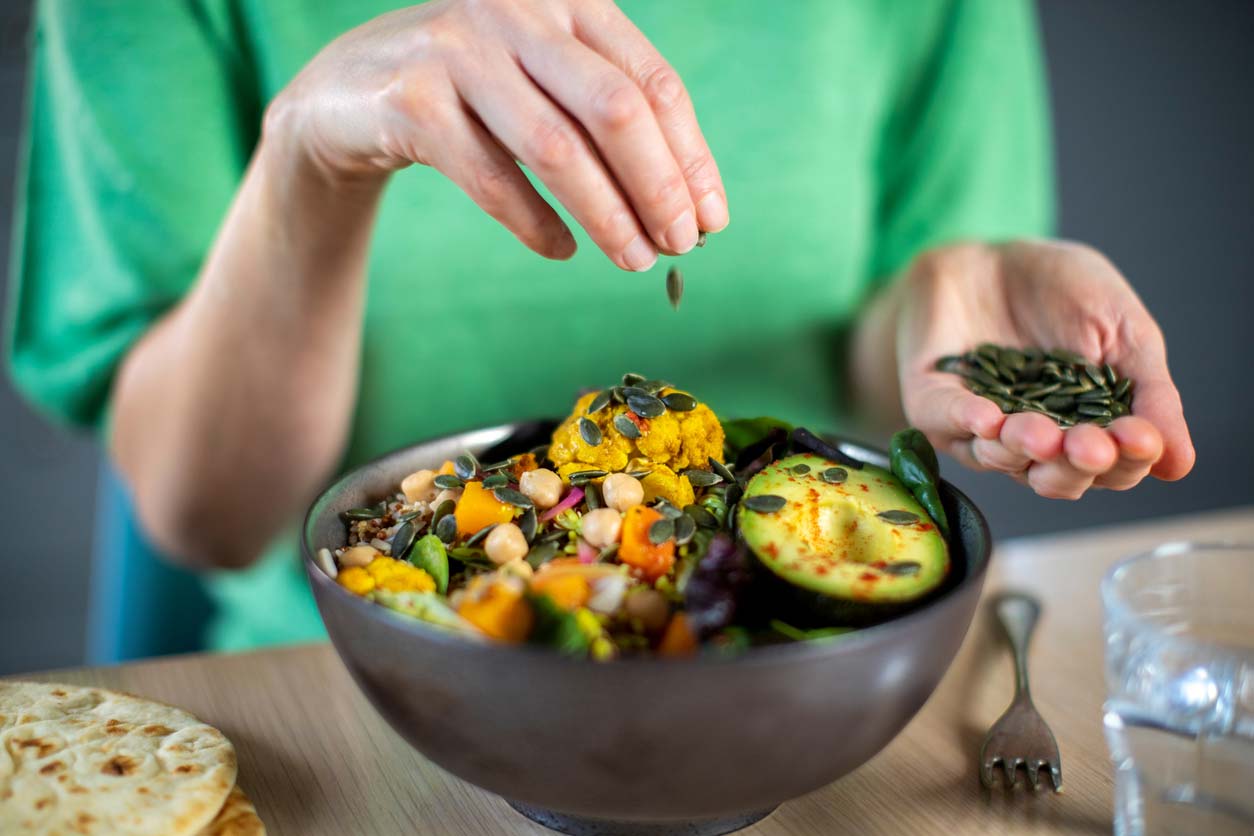 woman adding pumpkin seeds to vegan meal