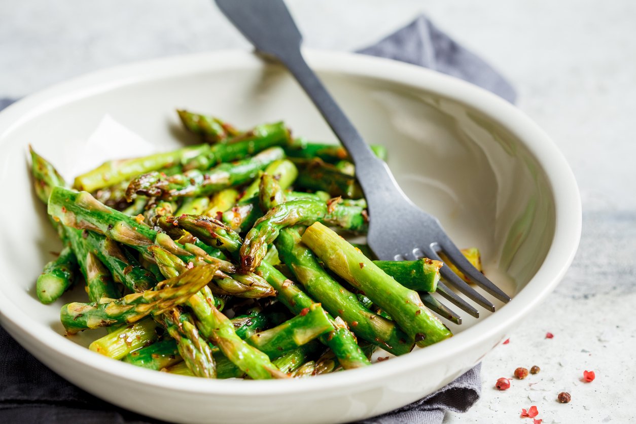 Green asparagus with pepper and salt in a white bowl.