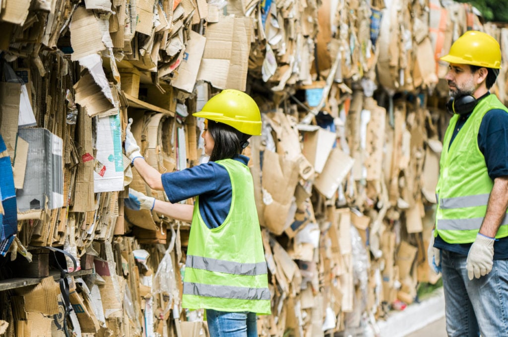 Male and female are working at waste management factory that recycles cardboard.
