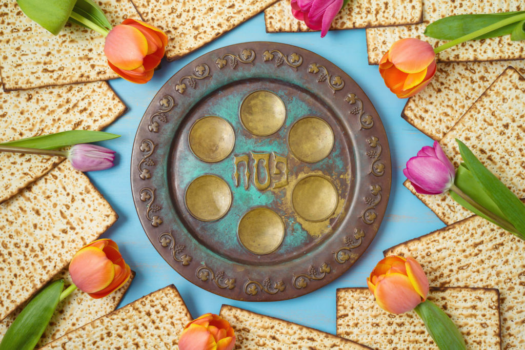 Jewish holiday Passover celebration concept with seder plate, matzah and tulip flowers on wooden table. Pesach background