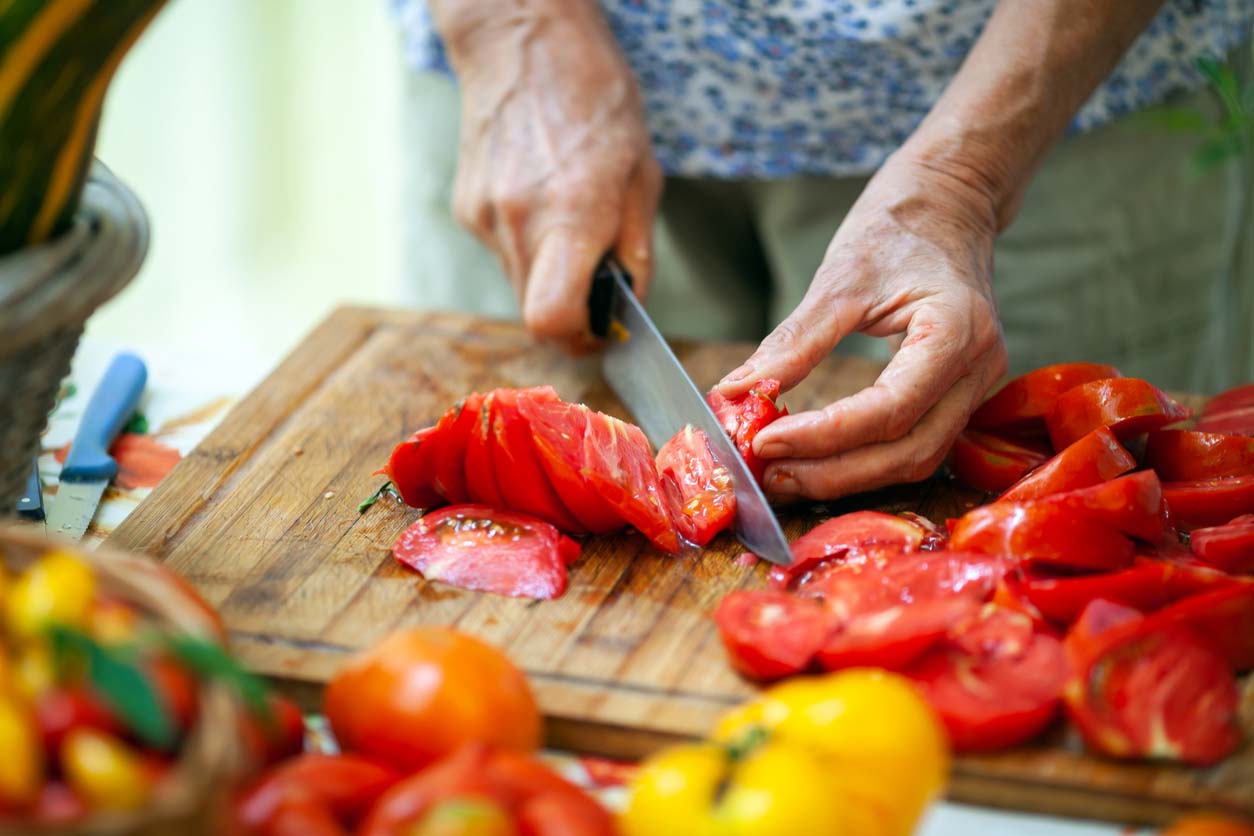 closeup of elderly woman slicing tomatoes on cutting board