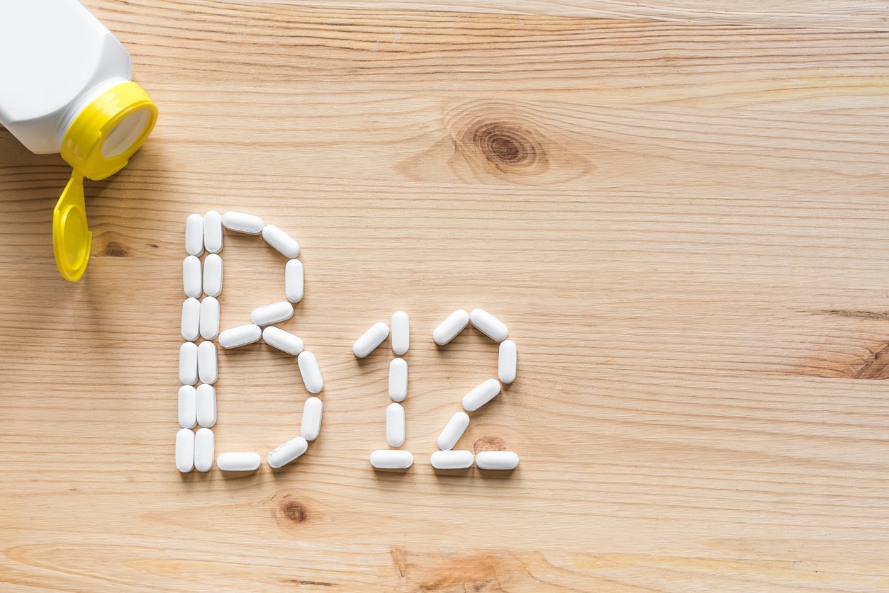 B12 Vitamin. White pills forming shape to B12 alphabet on wooden background, copy space, top view.