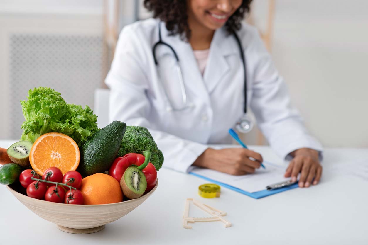 doctor writing out a produce prescription with bowl of fresh fruits and vegetables on desk