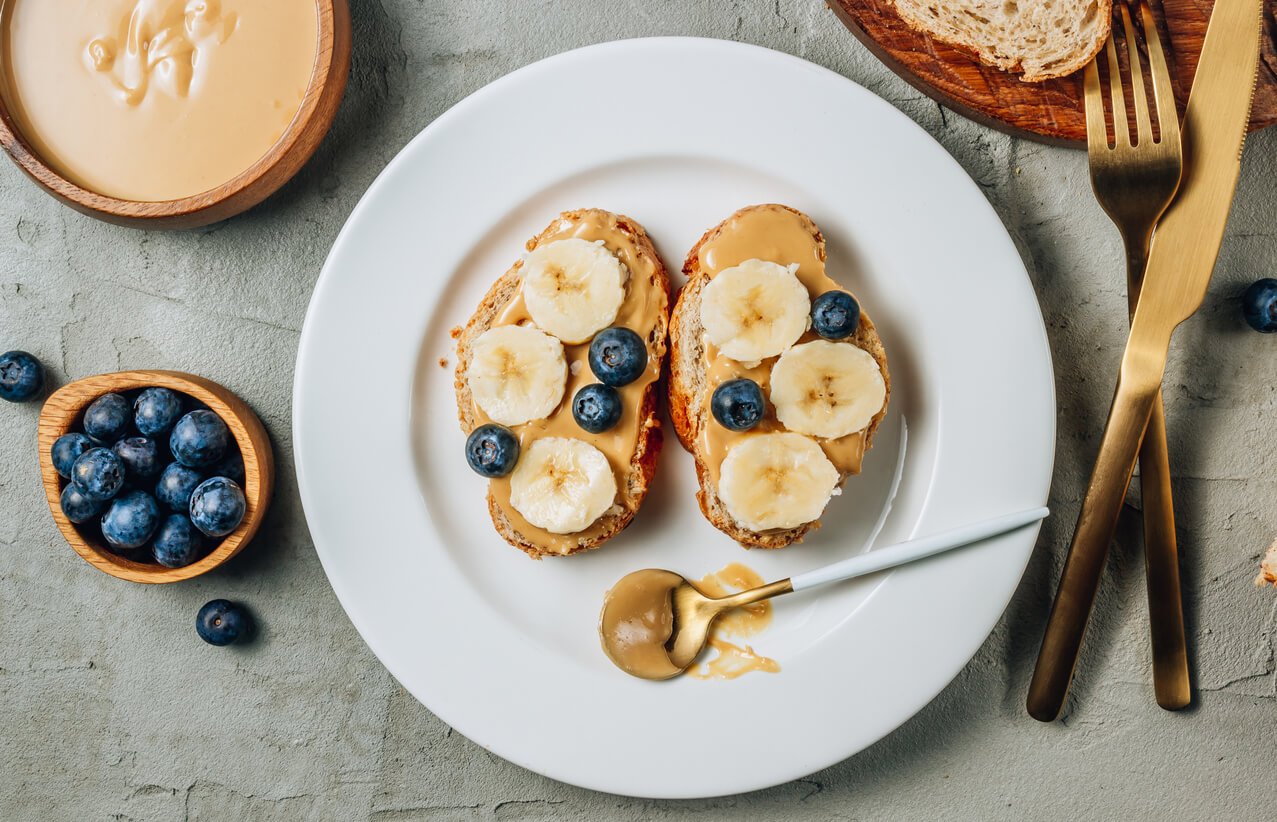buckwheat healthy bread with peanut butter banana and blueberry on white plate over