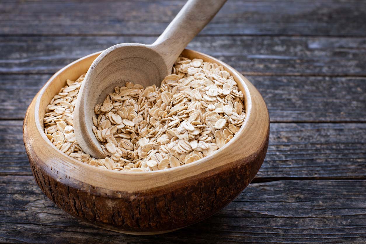 Oats in wooden bowl being scooped with wooden spoon