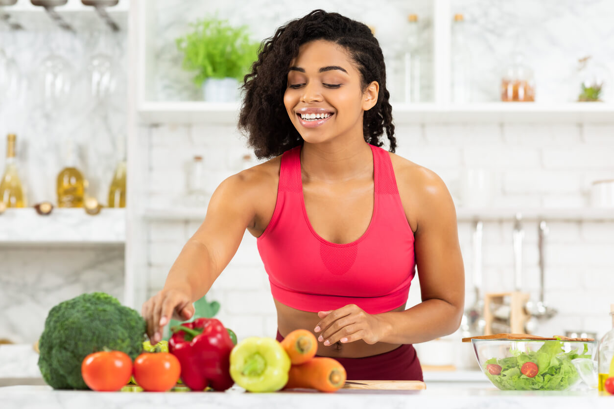 happy young black woman preparing vegetable salad