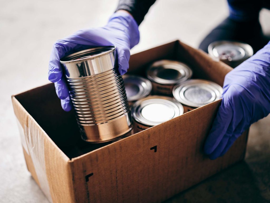 Gloved hands putting cans in a box for a food bank donation
