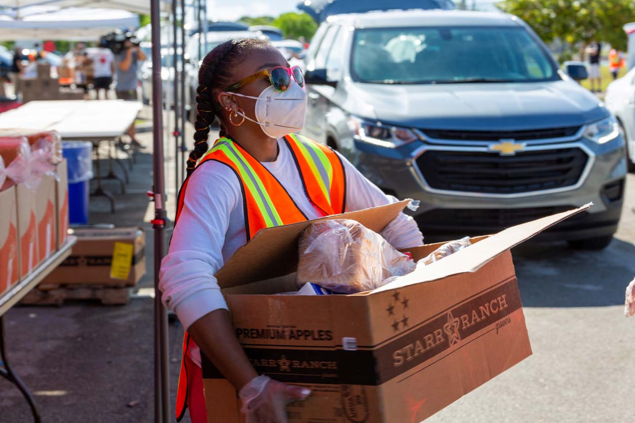 Woman volunteer carrying box of food to drive-thru food pantry