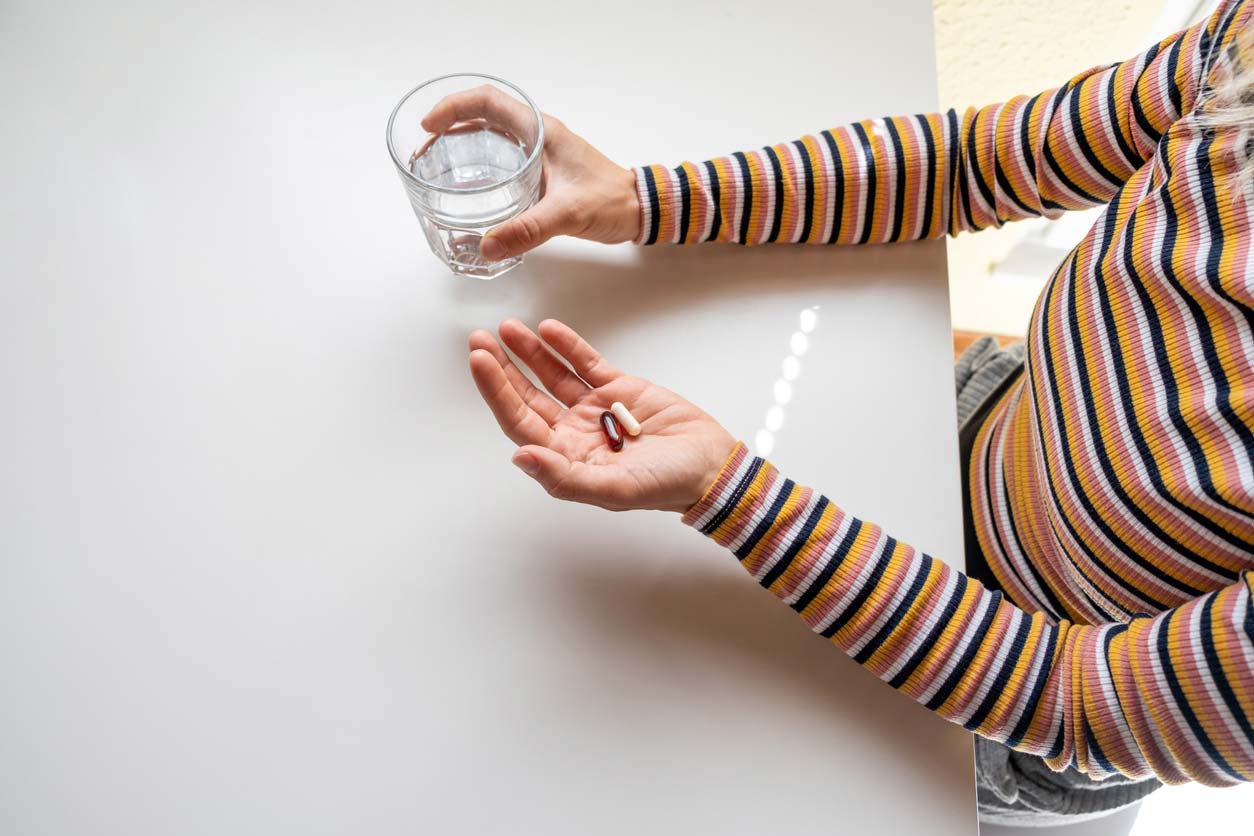 close up of supplements and water glass in hands of woman