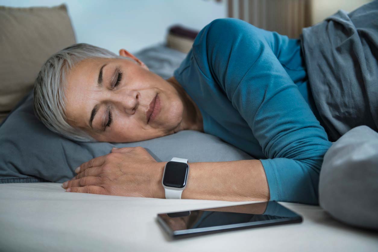 woman sleeping with health tracker on wrist and phone next to pillow