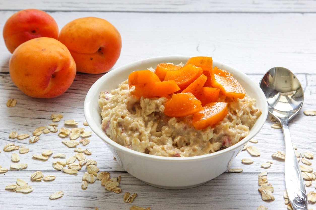 Oatmeal porridge with fresh apricots on a wooden background. Porridge in white plate with sliced apricots. Healthy breakfast.