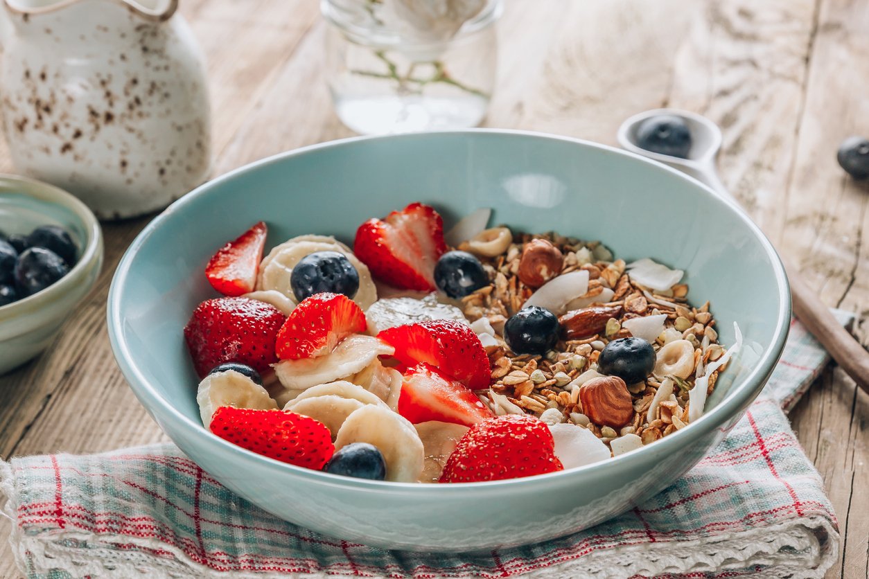 Healthy breakfast bowl with oat granola with dried buckwheat, nuts and coconut chips, berries and rice milk