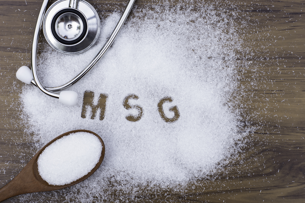 Monosodium glutamate (MSG ), ingredients in wooden spoon and words " MSG " with medical stethoscope isolated on the wood table background. Unhealthy food concept. Top view. Flat lay