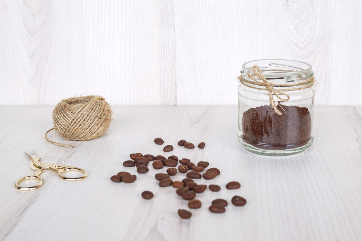 Ground coffee in a small glass jar decorated with jute thread, coffee beans; scissors an ball of jute thread on the wooden table. Concept of hand made natural air freshener