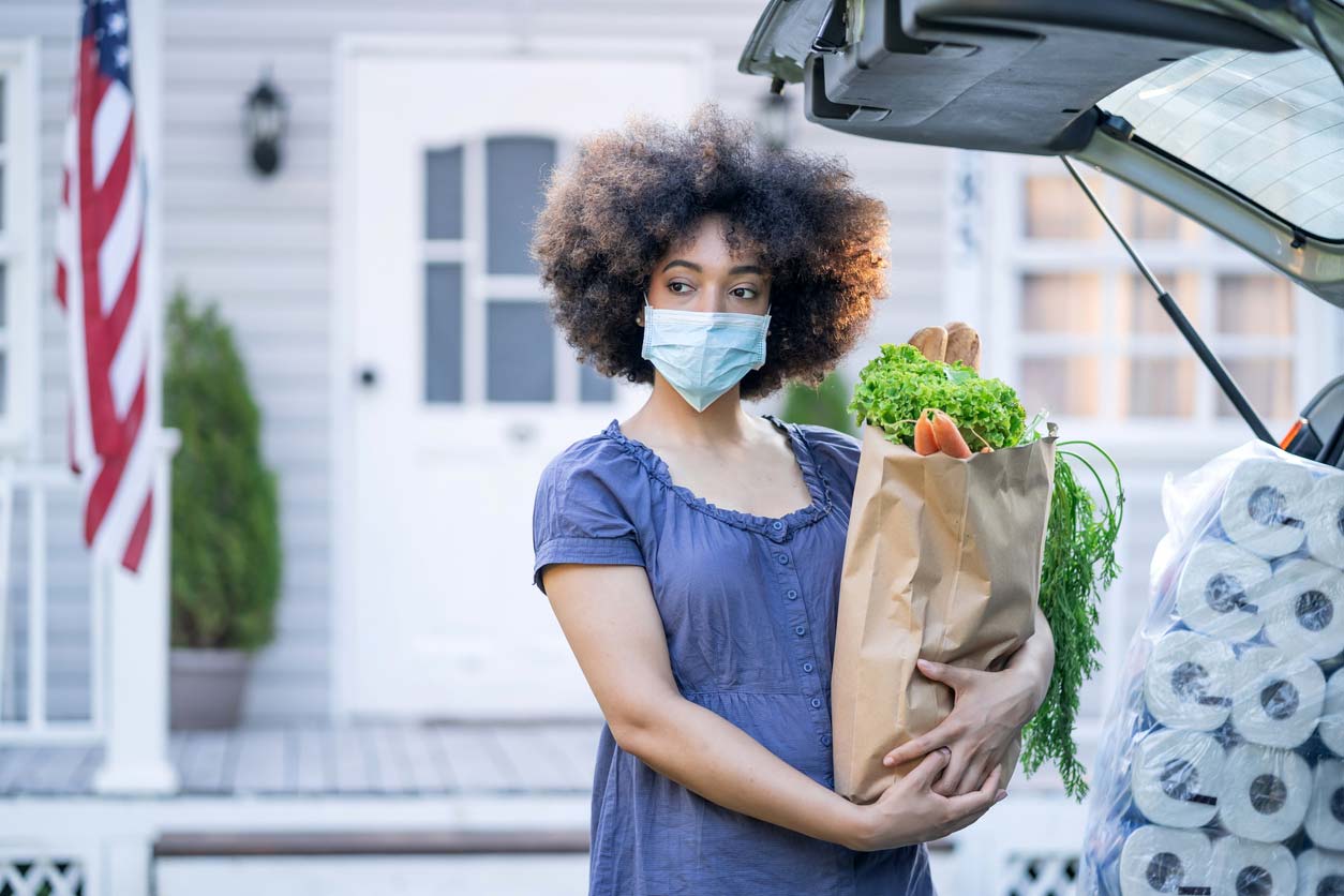 woman in mask holding groceries at back of vehicle