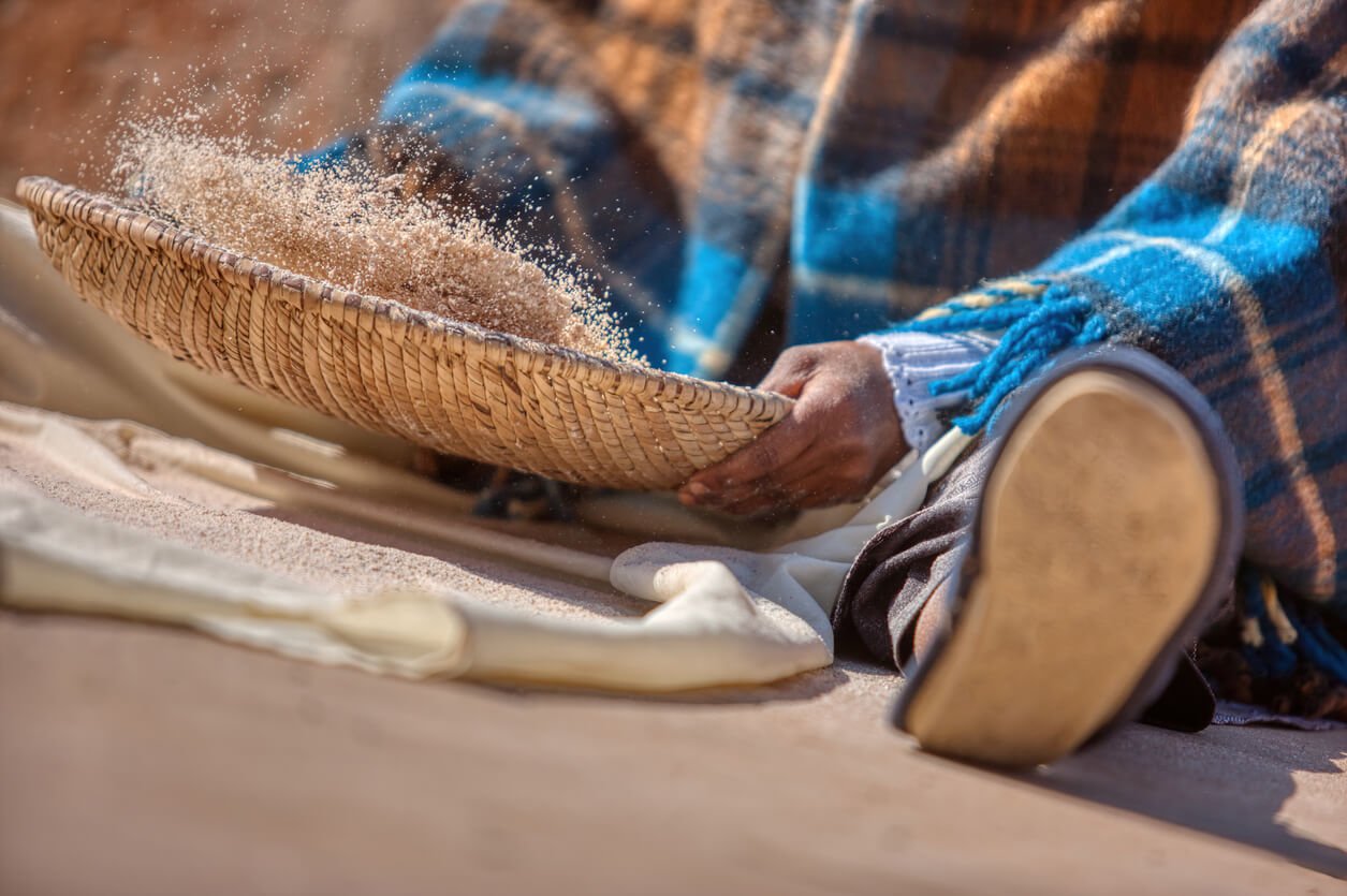 African woman using a handmade strainer to prepare the flour