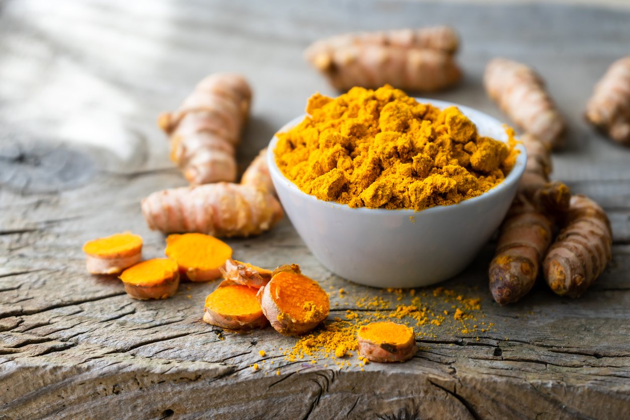 Turmeric powder in a white bowl and roots on a wooden table