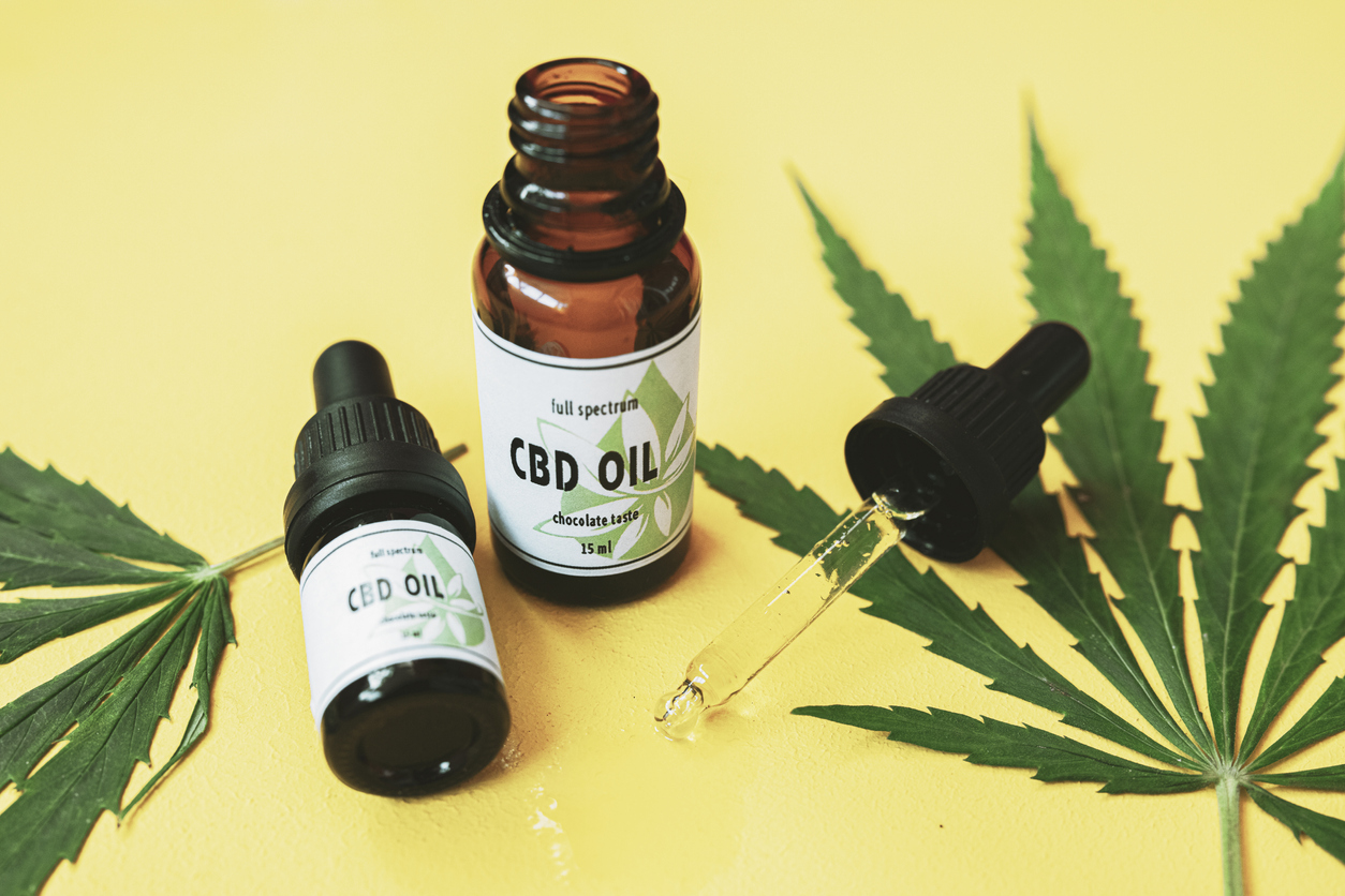 CBD oil and cannabis leaf on yellow background.