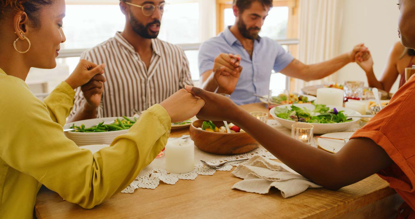 Diverse group saying grace around a table