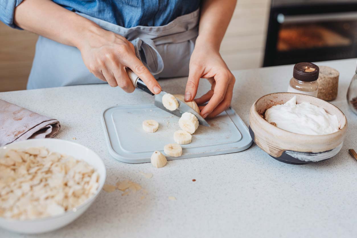 woman cutting banana to use as a topping on plant-based yogurt