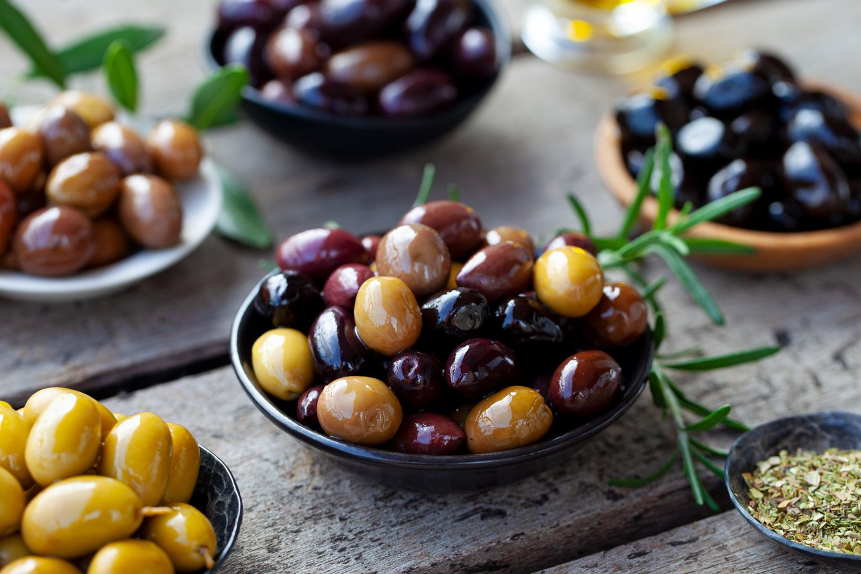 Assortment of fresh olives on a plate with olive tree brunches. Wooden background. Close up.