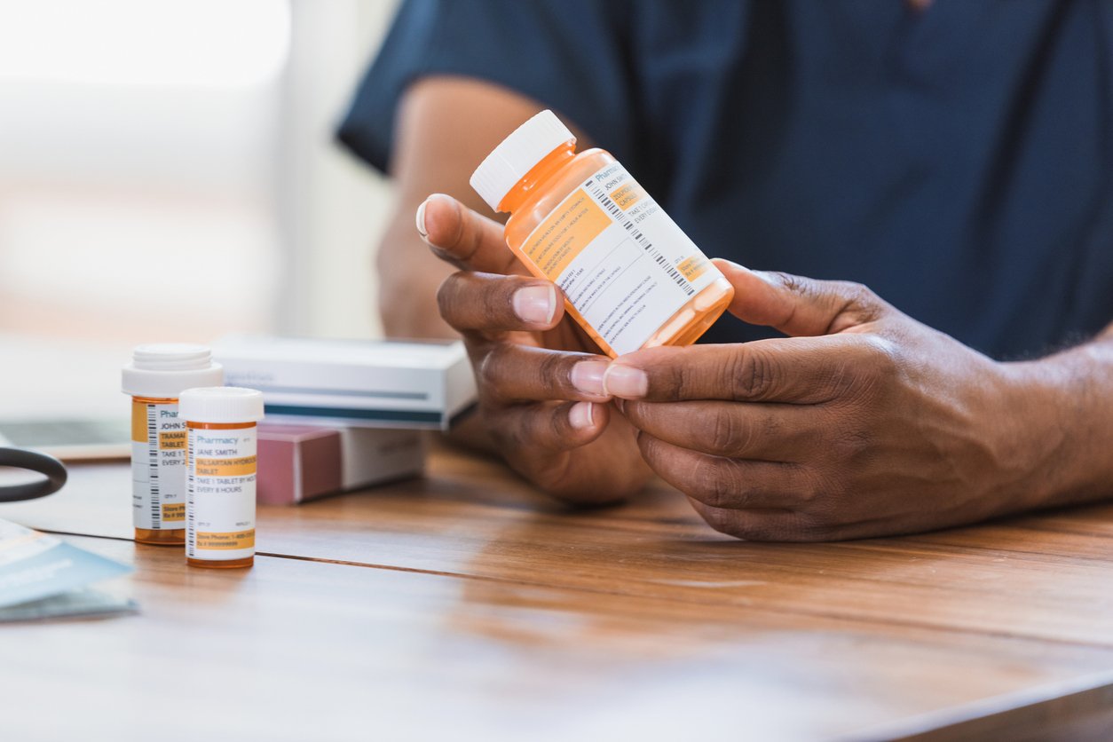 An unrecognizable male nurse reads a label on a prescription medication container.