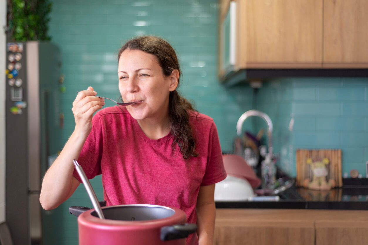 woman tasting cooked food on kitchen spoon 