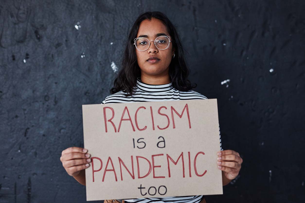 woman holding sign saying racism is a pandemic too