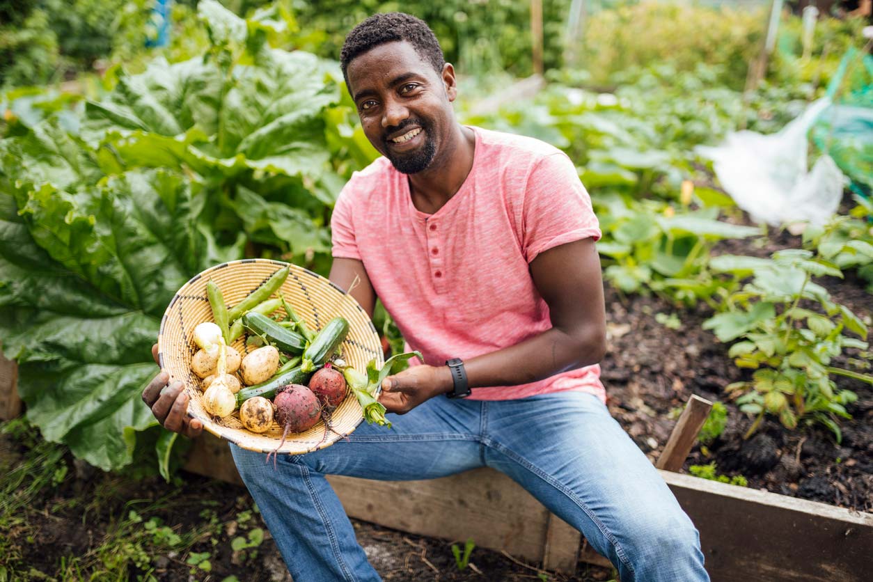 man holding basket of fresh vegetables from a community garden